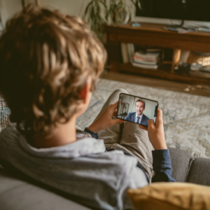 A student is holding a cell phone on a video call with a man in a shirt and tie.