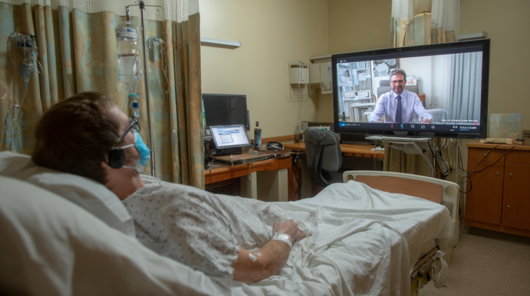 A man from a bed is having a visit via videoconference.
