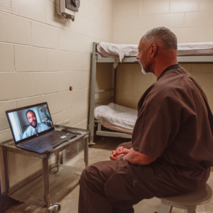 A prisoner is facing the wall on a video conference with a doctor.
