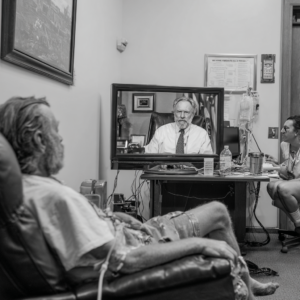 Black and white image of old man watching doctor on tv.
