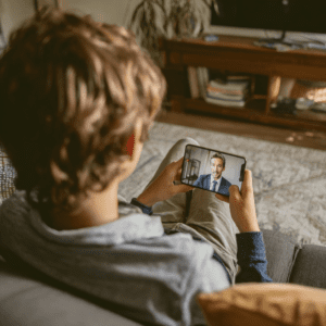 A student is holding a cell phone on a video call with a man in a shirt and tie.