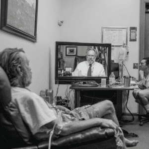 Black and white image of old man watching doctor on tv.